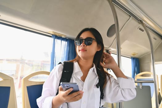 Happy young woman in sunglasses sitting inside public bus transport, enjoying travel transportation trip.