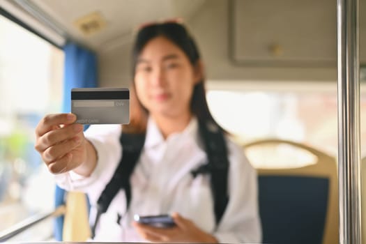 Young Asian woman showing credit card while sitting inside public bus transport.