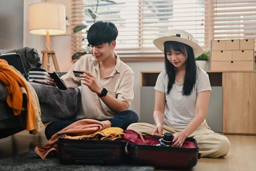 Happy young couple packing clothes into travel bag, getting ready for their holiday trip.