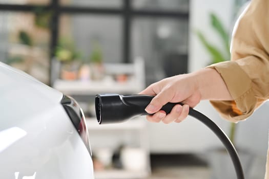 Man plugging the charging cable into his electric car. Renewable energy, sustainability and transport concept.