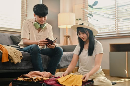 Young couple sitting on floor in living room and packing clothes into travel bag.