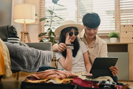 Cheerful couple holding credit card and making hotel reservation on digital tablet.