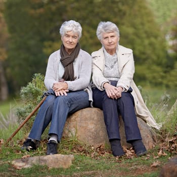 Senior friends, portrait or outdoor in nature on rock, together or bonding on retirement on holiday. Elderly women, serious or face on trip in countryside, winter or care for person with disability.