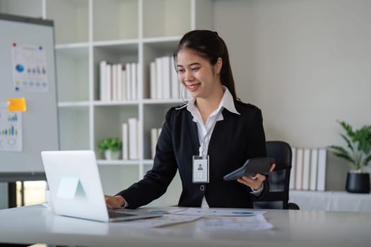 Charming Asian business woman sitting working on laptop in office.