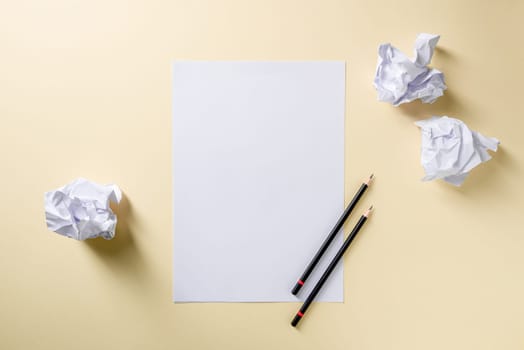 Blank writing sheet with pen and crumpled paper balls lay flat on yellow background