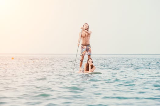 Sea woman and man on sup. Silhouette of happy young woman and man, surfing on SUP board, confident paddling through water surface. Idyllic sunset. Active lifestyle at sea or river