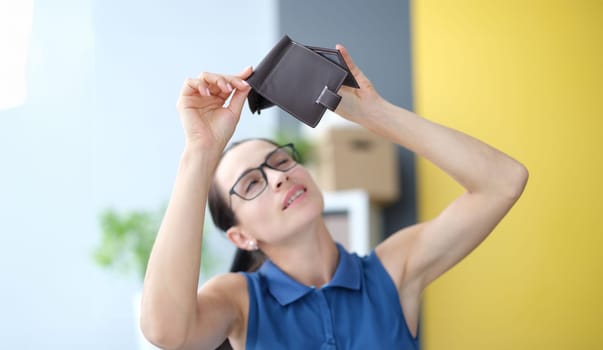 Young woman with glasses looking empty wallet at home. Economic crisis concept