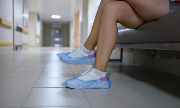 Woman in shoe covers sitting in hospital corridor closeup. Sanitary norms of behavior in medical institutions concept