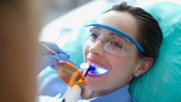 Woman in safety glasses undergoing treatment at dentist using led light lamp. Modern technologies in dentistry concept