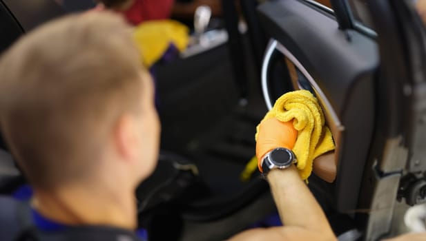 Male cleaner wiping dust in interior of car with microfiber cloth closeup. Car dry cleaning concept