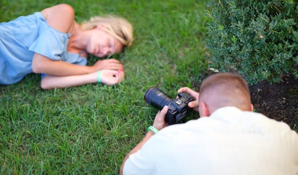 Man photographing young woman sleeping on grass. Professional photo session in nature concept