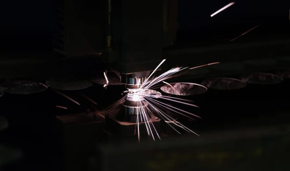 Laser machine cutting steel sheet with bright sparks closeup. Metalworking concept