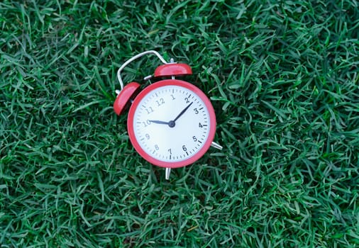 Red classic alarm clock lying on green grass closeup. Healthy lifestyle concept