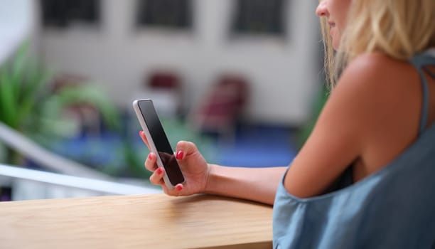 Young woman holding mobile phone in her hands and looking at screen closeup. Remote communication in social networks concept