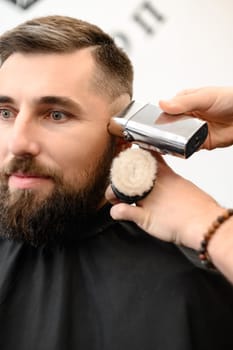 Barber shaves the temple with a cordless trimmer during a short haircut on the sides of the head.