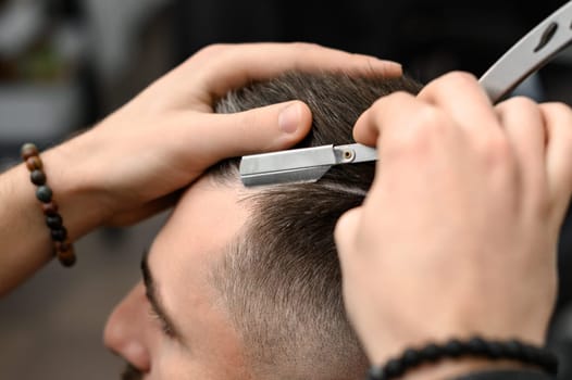 The barber makes the outline with a dangerous razor during the undercut haircut