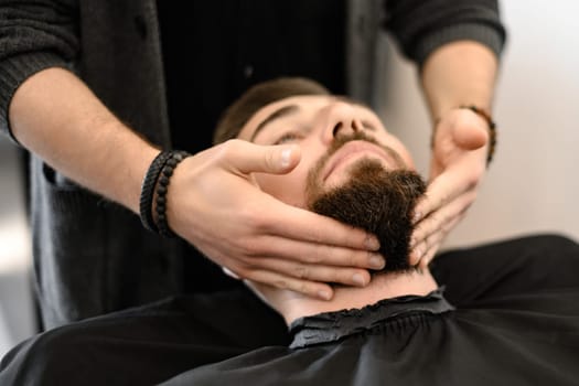 A barber massages and rubs a male clients beard after applying moisturizing oil
