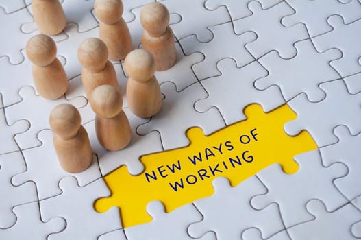 Empty jigsaw puzzle with text - new ways of working surrounded by wooden figures. Business culture.