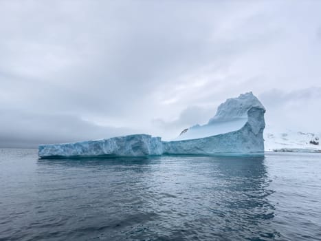 A huge high breakaway glacier drifts in the southern ocean off the coast of Antarctica at sunset, the Antarctic Peninsula, the Southern Arctic Circle, azure water, cloudy weather. High quality photo