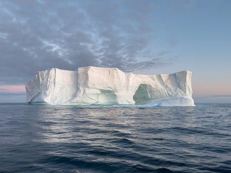 A huge high breakaway glacier drifts in the southern ocean off the coast of Antarctica at sunset, the Antarctic Peninsula, the Southern Arctic Circle, azure water, cloudy weather. High quality photo