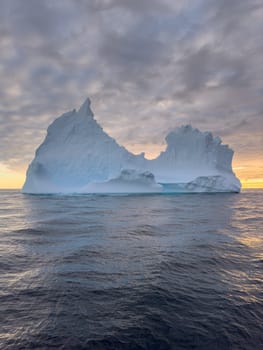 A huge high breakaway glacier drifts in the southern ocean off the coast of Antarctica at sunset, the Antarctic Peninsula, the Southern Arctic Circle, azure water, cloudy weather. High quality photo