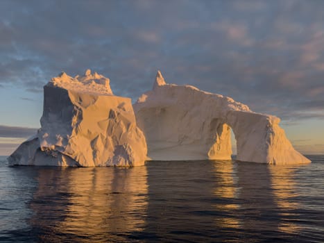 A huge high breakaway glacier drifts in the southern ocean off the coast of Antarctica at sunset, the Antarctic Peninsula, the Southern Arctic Circle, azure water, cloudy weather. High quality photo