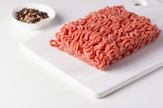 Fresh raw minced meat and peppers on a white table, close-up.