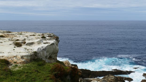 Coast of the sea with waves crashing on the rocks. Mount with grass and limestone.