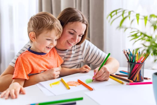 A caring mother supporting her laughing son as they draw together, surrounded by a colorful array of pencils.
