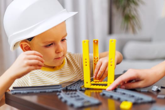 A focused child wearing a hard hat plays with a construction toy set indoors.