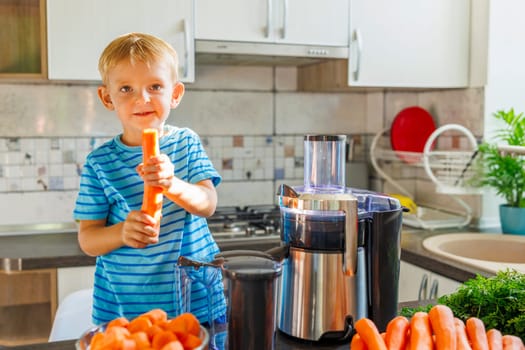 A smiling young boy prepares carrot juice using a juicer in a sunny kitchen.
