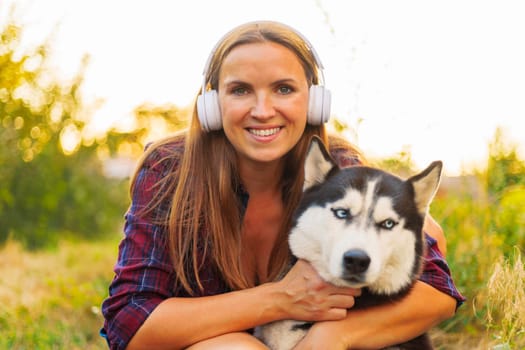 In a golden hour glow, a smiling woman warmly embraces her loyal Husky dog while enjoying a serene outdoor setting.