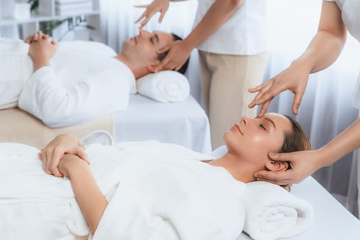 Caucasian couple enjoying relaxing anti-stress head massage and pampering facial beauty skin recreation leisure in dayspa modern light ambient at luxury resort or hotel spa salon. Quiescent