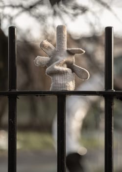Forgotten glove hanging on a metal fence railing with the middle finger up. A lost glove artistically placed on black metal fence post with blurred background, Space for text, Selective focus.