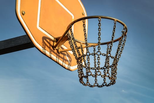 Edinburgh, Scotland, Jan 19, 2024 - Side view of Basketball backboard with the hoop metal ring and steel chain net against blue sky background seen from below. Street basketball court, Low angle view, Look up, Space for text, Selective focus.