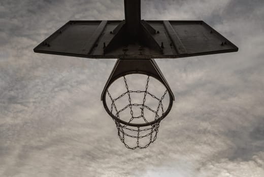 Edinburgh, Scotland, Jan 19, 2024 - Steel basketball backboard with the hoop metal ring and steel chain net against sky background seen from below. Street basketball court, Low angle view, Look up, Space for text, Selective focus.