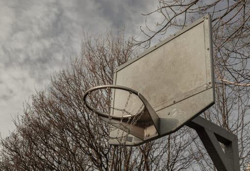 Edinburgh, Scotland, Jan 19, 2024 - Side view of Steel basketball backboard with the hoop metal ring and steel chain net against branches and sky. Street basketball court, Space for text, Selective focus.