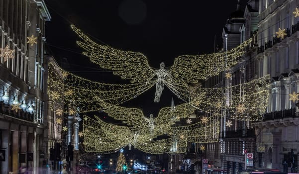 London, UK - Dec 25, 2023 - Flying angel Christmas decoration led lights display. Dramatic view of the traditional Christmas decoration lights hanging above Regent Street during dusk, The Spirit of Christmas, Light Festival in London, Space for text, Selective focus.