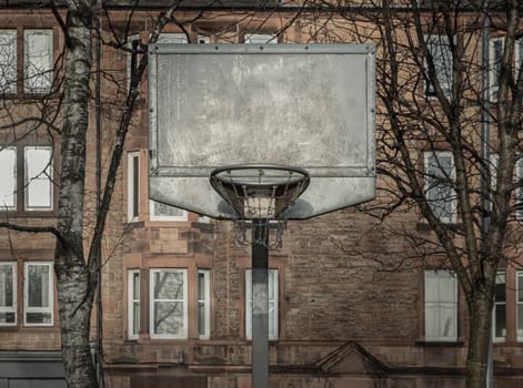Edinburgh, Scotland, Jan 19, 2024 - Steel basketball backboard with the hoop metal ring and steel chain net at outdoor basketball courts with old buildings background in the city downtown. Space for text, Selective focus.
