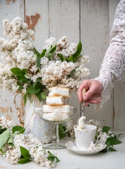 woman preparing a cold coffee dessert, spring still life in retro style, a stack of waffle ice cream in a bowl with a bouquet of white lilacs in an antique teapot, high quality photo