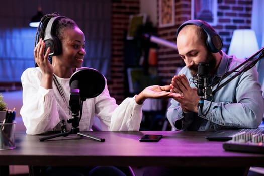 Cohosts presenting religion podcast in professional studio, teaching prayers to audiences. Presenter using high quality recording setup to film spirituality conversation, doing hands together gesture