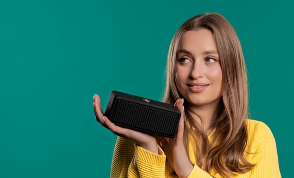Woman dancing, enjoying on blue studio background. Girl moves to rhythm of music. Young teenager listening to music by wireless portable speaker - modern sound system. Copy space.