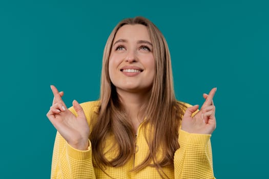 Student praying with crossed fingers on blue background. Woman begs someone satisfy desires, help with, prays for luck in exam. High quality