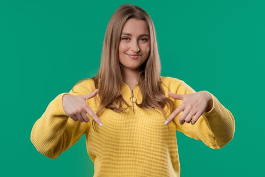 Pretty woman pointing down to advertising area. Blue background. Young lady asking to click to subscribe below. Copy space for your commercial idea, promotional content. High quality photo