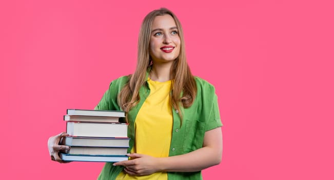 Smiling student woman with stack books from library, pink background. Copy space. Happy girl smiles, she is happy to graduate. High quality