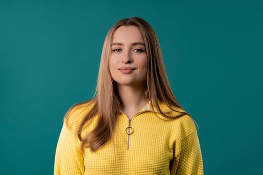 Young portrait woman in yellow sweater looking to camera on blue studio background. Pretty blonde female smiling model.