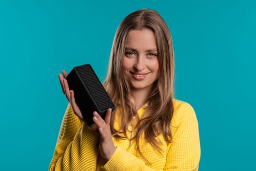 Woman dancing, enjoying on blue studio background. Girl moves to rhythm of music. Young teenager listening to music by wireless portable speaker - modern sound system. Copy space.