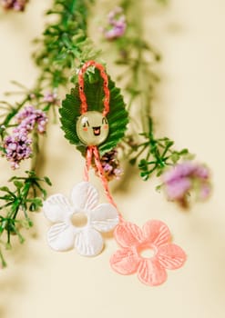 One beautiful homemade martisor of two flowers, a petal and a cheerful smiley face with a bouquet of spring flowers lies on a pastel yellow background, close-up side view.