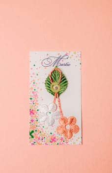 One beautiful homemade martisor of two flowers, a petal and a cheerful smiley face lies on a small colorful paper with the inscription martie on a pink background, flat lay close-up.