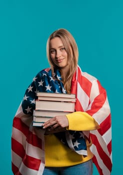 American woman student holds stack of university books from college library on blue background. Happy girl smiles, she is happy to graduate in USA, education abroad concept